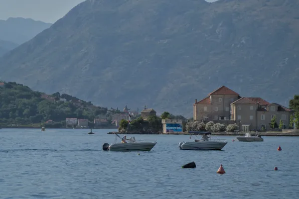 Deux bateaux sur les eaux bleues calmes de la baie de Kotor, Monténégro, avec un village et des montagnes à l'arrière-plan.