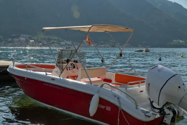 Un motoscafo rosso e bianco giace nell'acqua scintillante di un porto a Kotor, Montenegro, con colline verdi sullo sfondo.