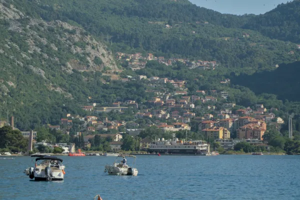 Blick auf die Bucht von Kotor mit Booten auf dem Wasser und einer Stadt, die sich an grüne Berghänge schmiegt.