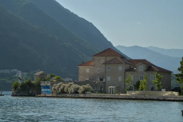 Bâtiment historique dans la baie de Kotor avec des montagnes à l'arrière-plan et une structure ressemblant à un phare.