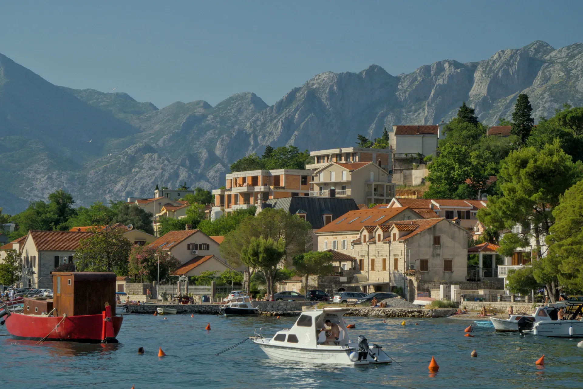 Prikaz Boke Kotorske sa šarmantnim kućama, čamcima i planinama u pozadini, koji dočarava scenu Dobro.