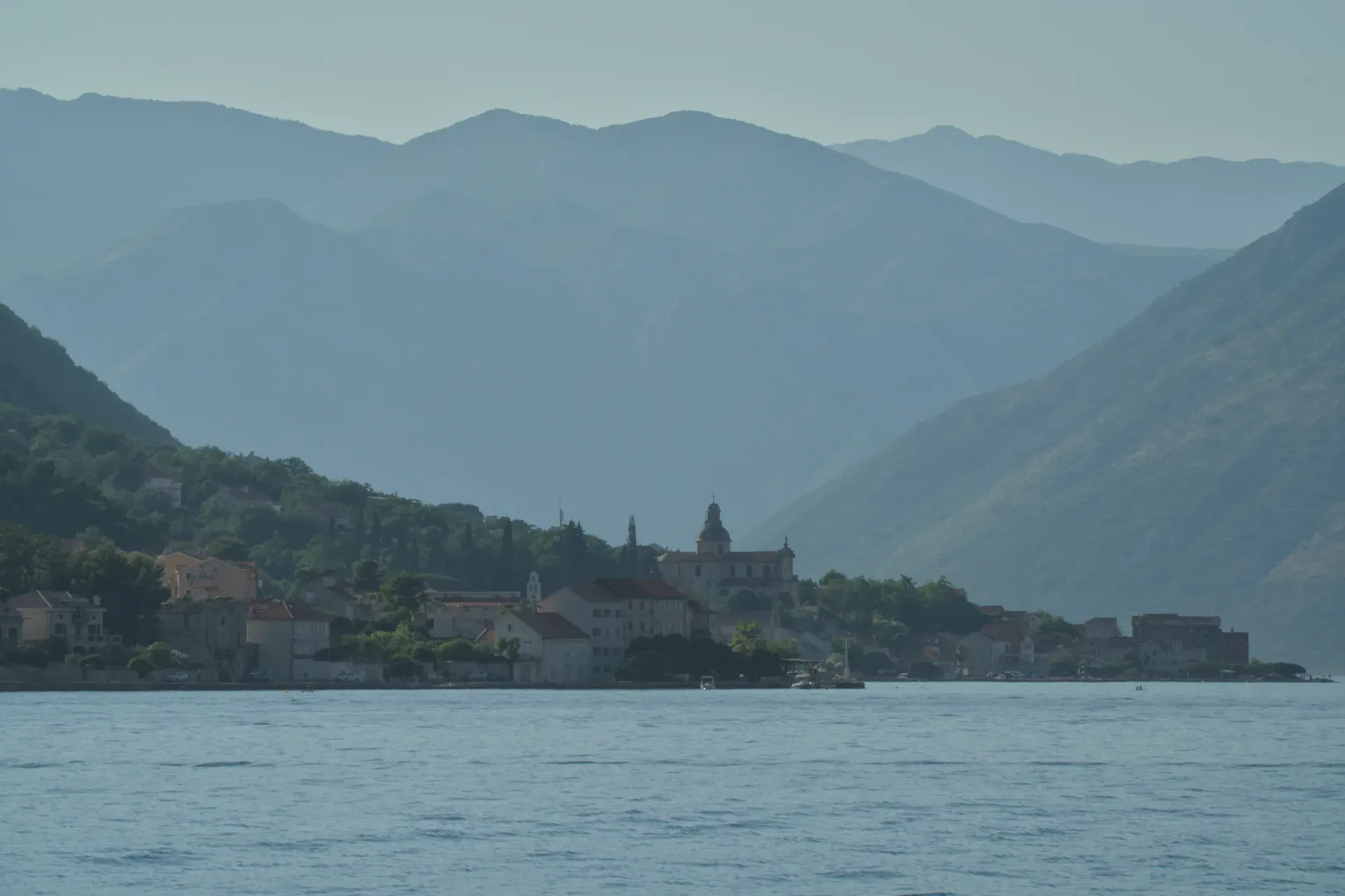 Küste von Kotor mit einer Stadt und Bergen im Hintergrund, eingefangen aus der Wasserperspektive.
