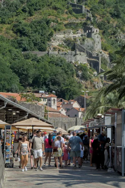 Una calle animada en el casco antiguo histórico de Kotor, Montenegro, con antiguas murallas de piedra y ruinas de fortalezas en la cima de una colina.