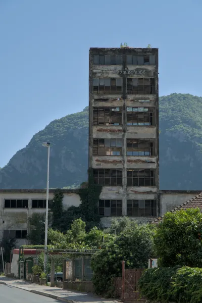 Ein verfallenes, mehrstöckiges Gebäude in Kotor, Montenegro, mit Fenstern und bergiger Landschaft im Hintergrund.