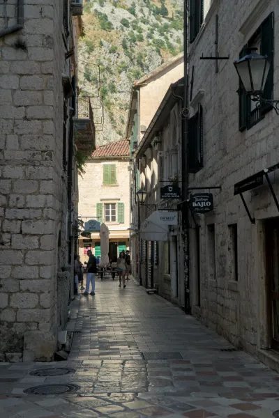 Sonnenbeschienene Gasse in der Altstadt von Kotor, Montenegro, mit Steingebäuden und Blick auf die Berge.