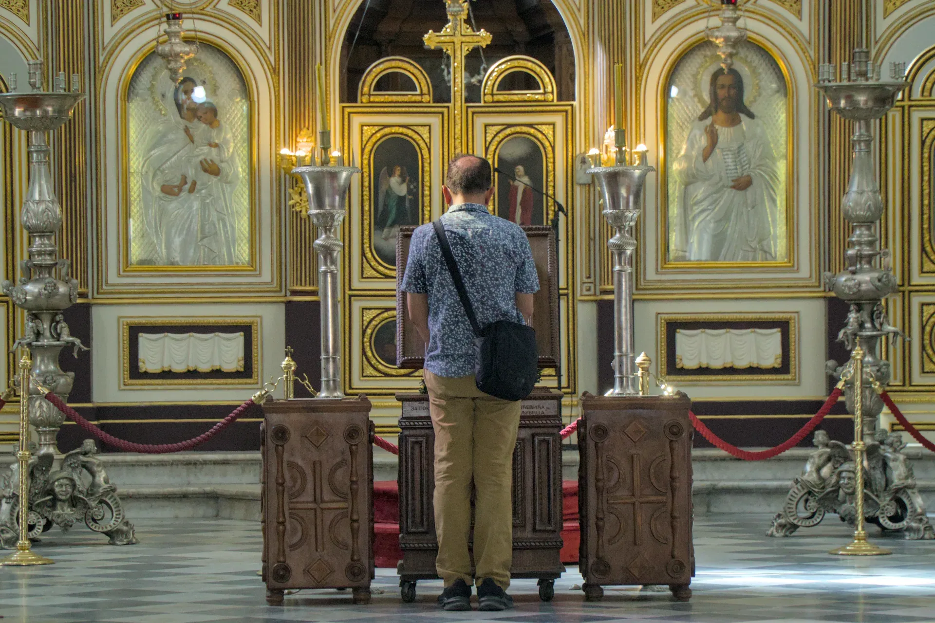Un hombre se para devotamente ante un iconostasio ortodoxo adornado con adornos dorados e iconos.