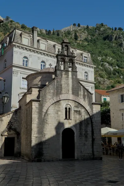 Un'antica chiesa in pietra con campanile e facciata ad arco si erge davanti a una fortezza di montagna a Kotor.