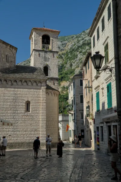 Uzak, popločan ulica u starom gradu Kotora, Crna Gora, sa istorijskim kamenim zgradama i crkvenim tornjem u pozadini.