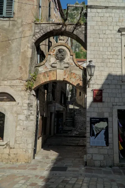 Ein alter Steinbogenweg in Kotor, Montenegro, mit Schatten und Licht auf den Pflastersteinen und Gebäuden.