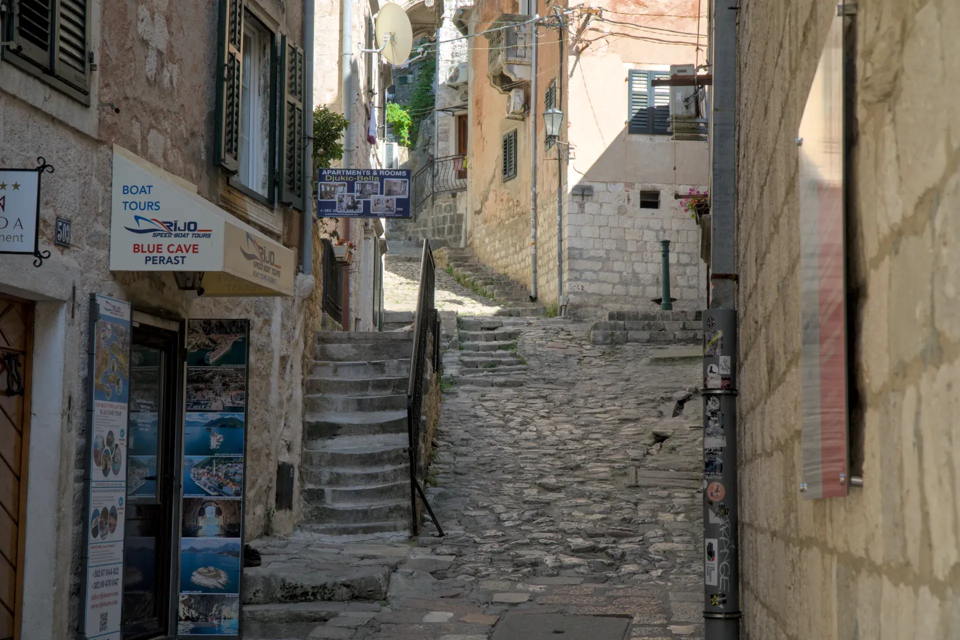 Eine steile, kopfsteingepflasterte Gasse in Kotor, Montenegro, mit steinernen Gebäuden und einer Steintreppe, die in die Höhe führt.