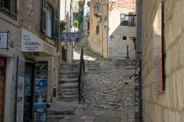 A steep, cobblestone alley in Kotor, Montenegro, with stone buildings and a stone staircase leading upwards.