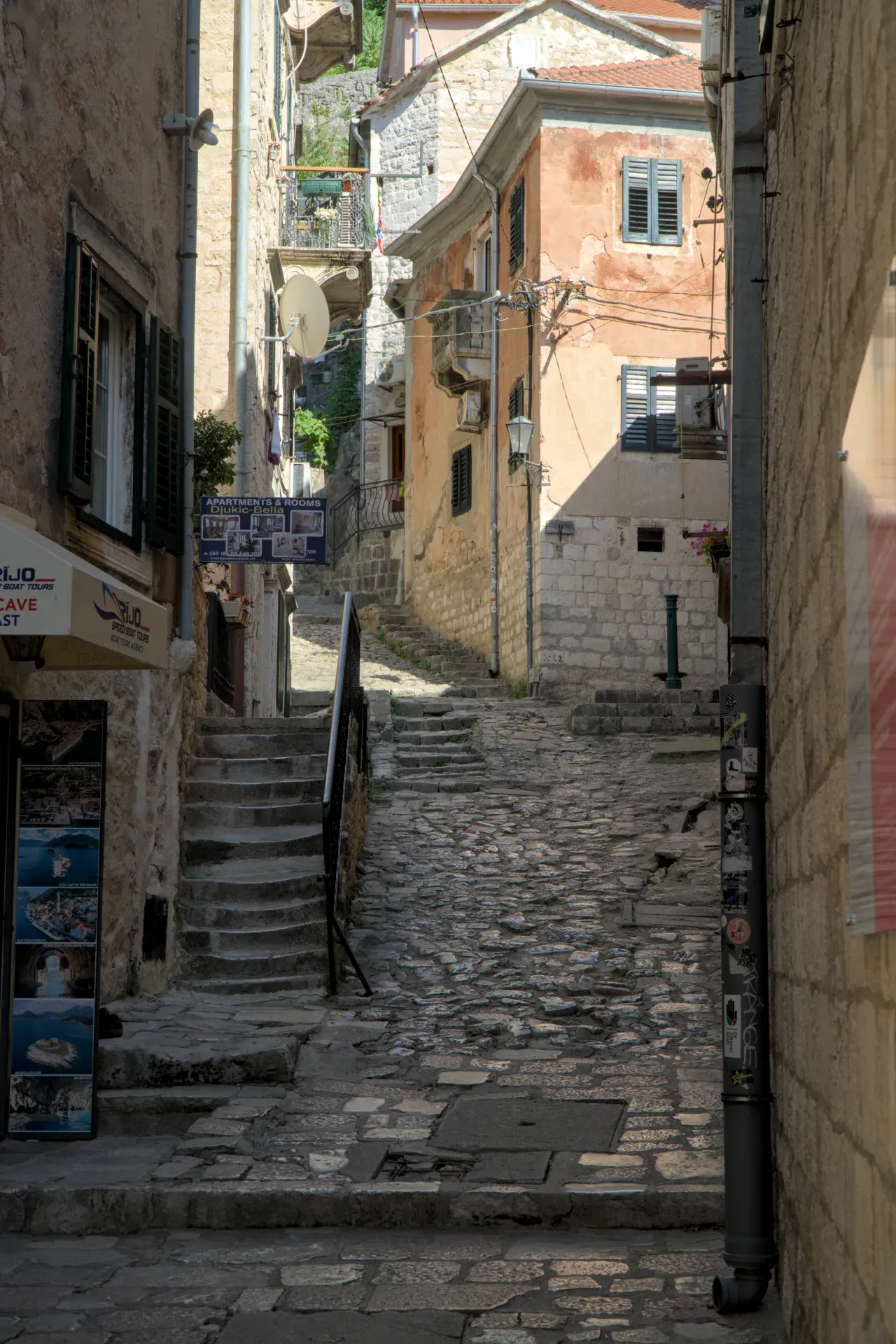 Une ruelle escarpée et pavée à Kotor, Monténégro, bordée de bâtiments historiques et d'escaliers en pierre, avec un jeu de lumière dramatique.