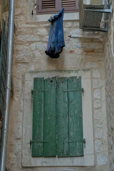 Una finestra con persiane verdi in legno e jeans appesi ad asciugare su un rustico muro di pietra a Kotor.