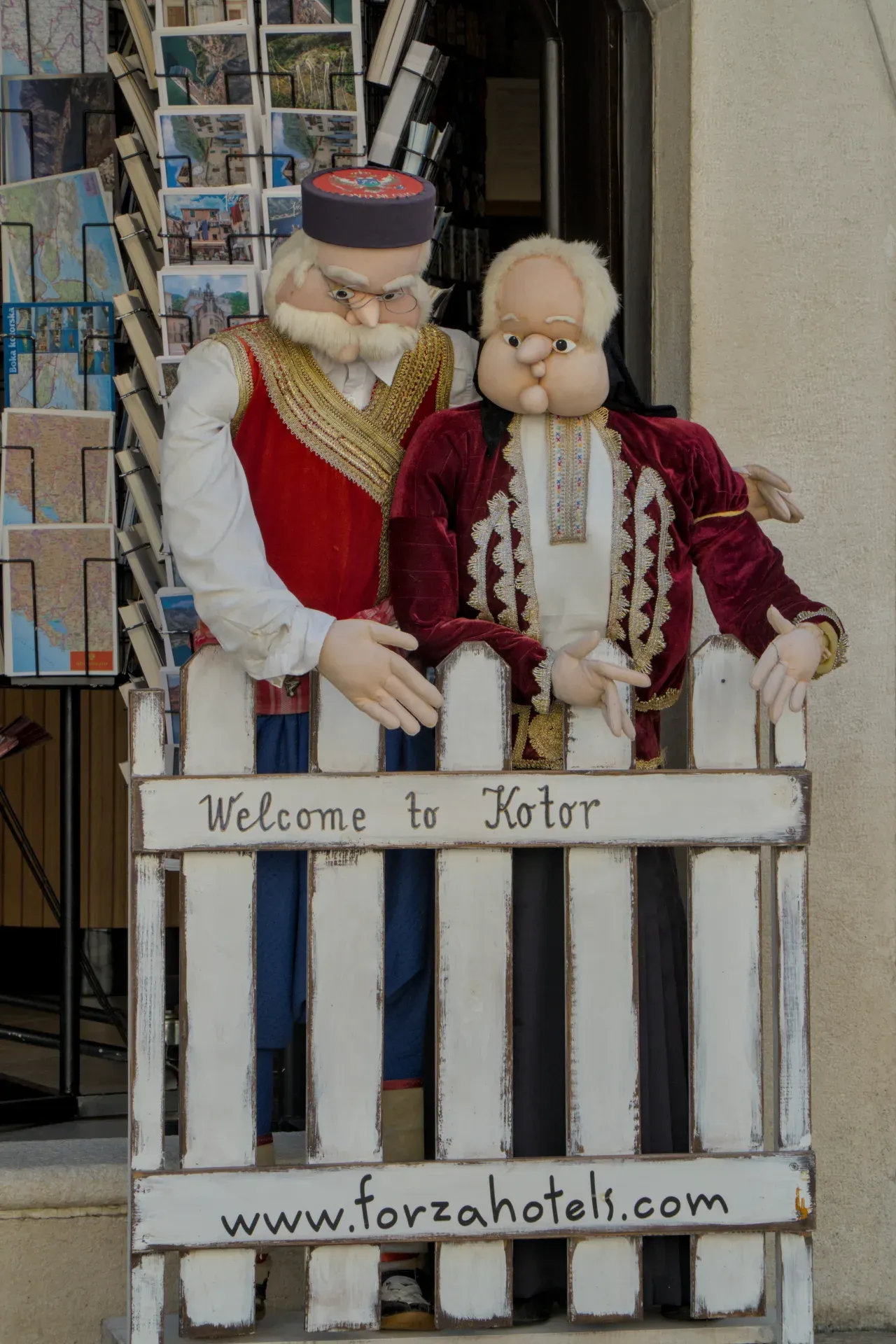 Tradicionalno obučene figure pozdravljaju posetioce ispred znaka "Welcome to Kotor" u Crnoj Gori.