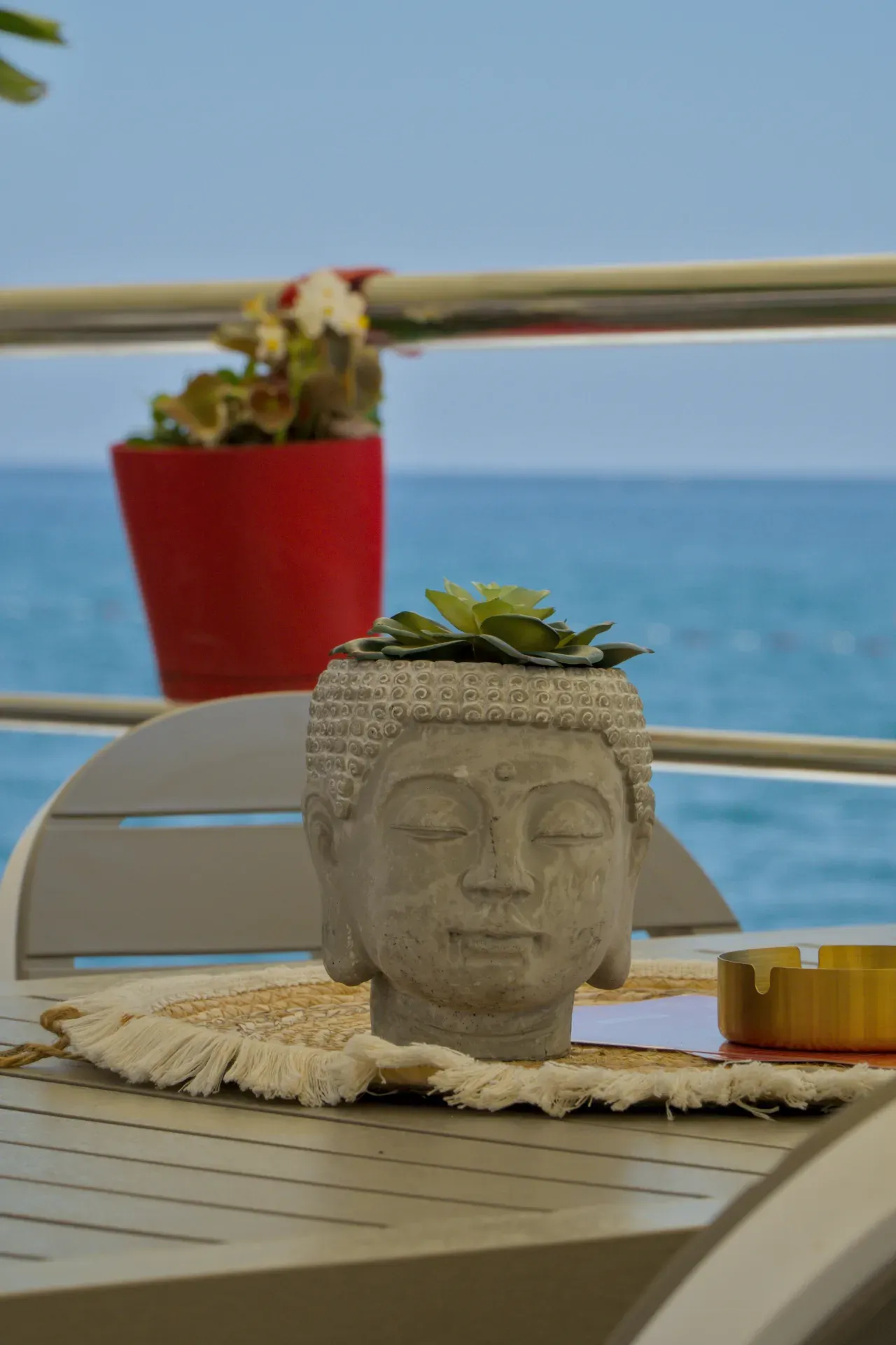 Buddha-Kopf-Blumentopf mit Sukkulente auf einem Tisch vor dem blauen Meer.