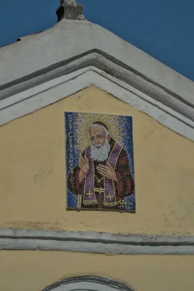 Mosaico dettagliato di un santo barbuto con veste viola su una facciata gialla a Herceg Novi, Montenegro.