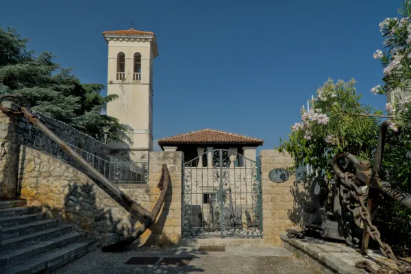 Una vecchia ancora arrugginita giace davanti a una scalinata di pietra, accanto un snello campanile.