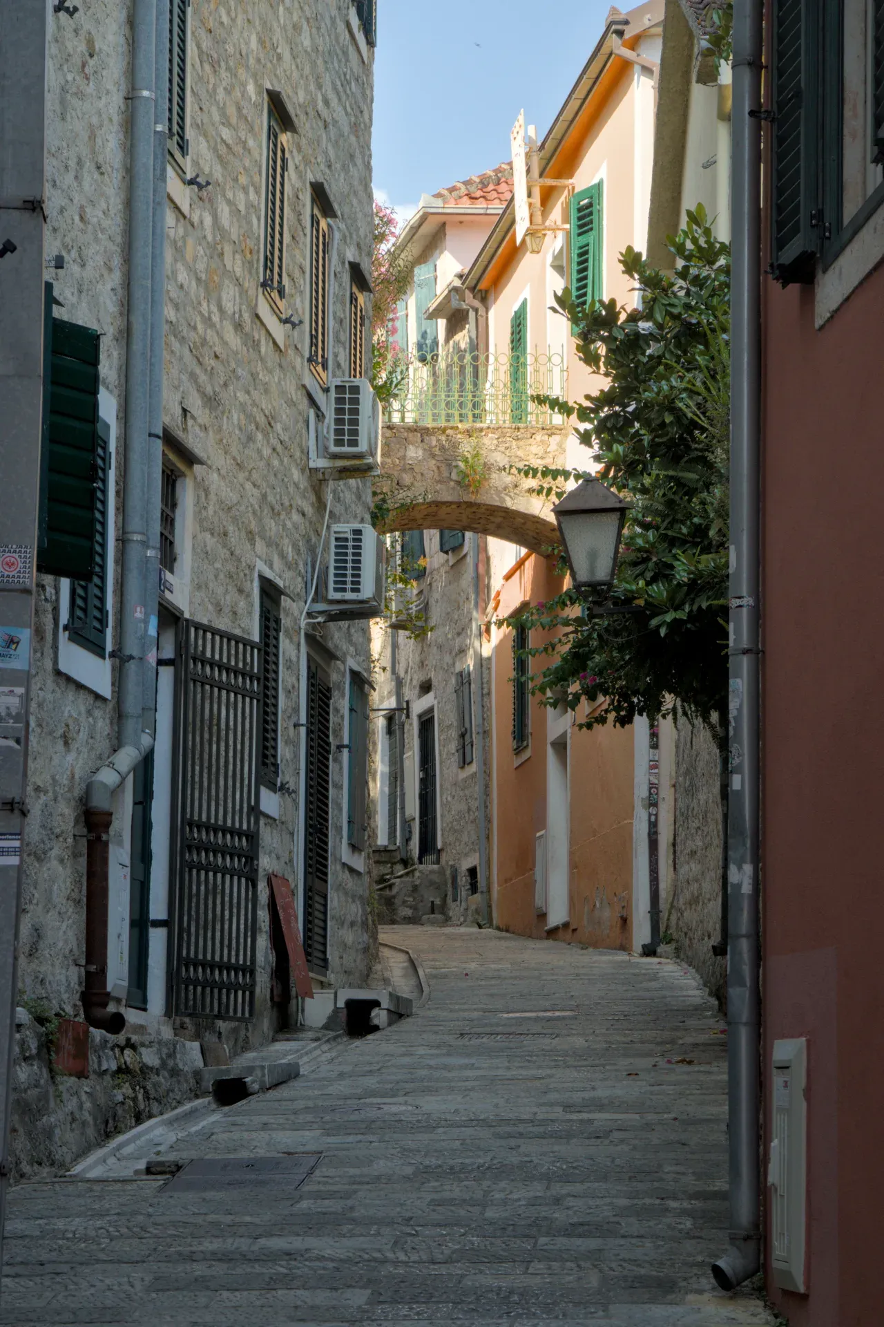 Un vicolo di pietra a Herceg Novi, Montenegro, con case antiche e un arco sopra, che invita all'esplorazione.