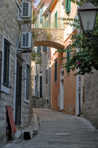 Uno stretto vicolo in pietra a Herceg Novi sotto un arco in pietra con edifici dai toni caldi.