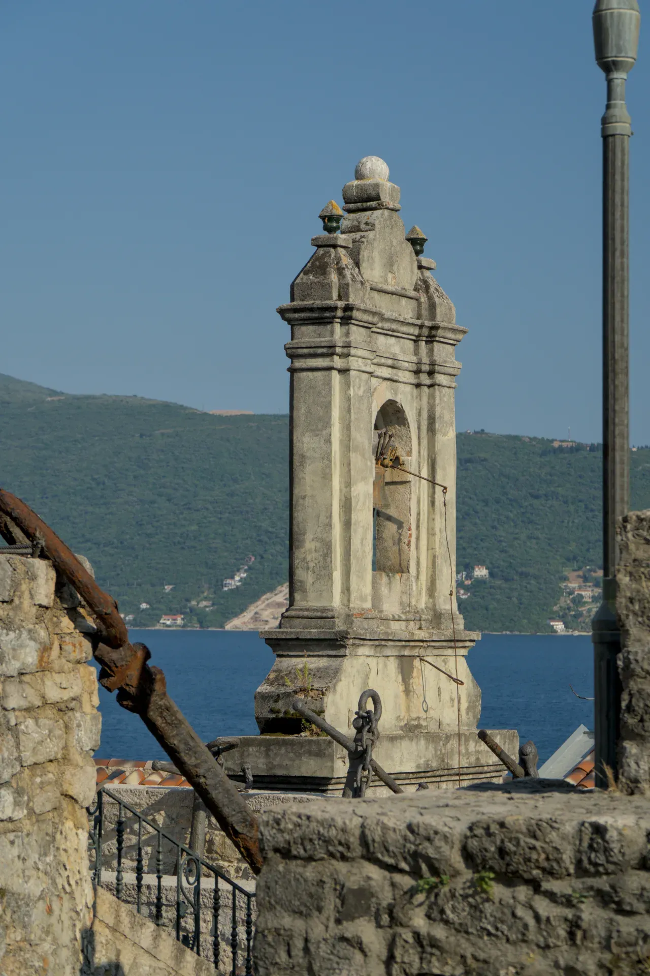 Un campanile in pietra consumato dal tempo affacciato sul mare a Herceg Novi, Montenegro, con ancore antiche.