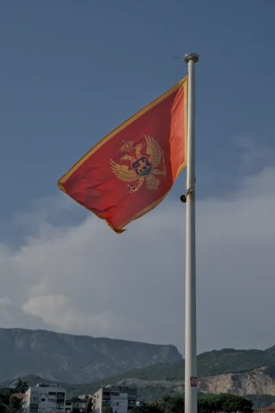 Bandiera del Montenegro con stemma che sventola al vento davanti a un cielo blu sopra Herceg Novi
