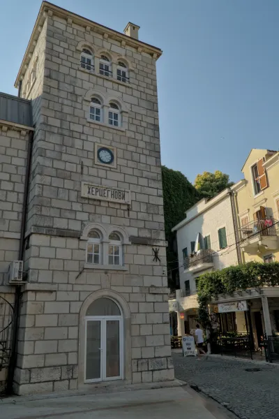 Una torre dell'orologio in pietra a Herceg Novi, Montenegro, con quadrante blu e iscrizione cirillica sopra un arco.