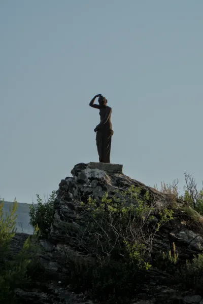 Statua in bronzo di una donna su uno sperone roccioso con cielo limpido a Herceg Novi.