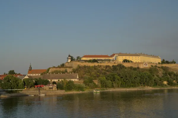 Petrowaradeiner Festung, Serbien, im warmen Abendlicht, mit Fluss und Bäumen im Vordergrund.