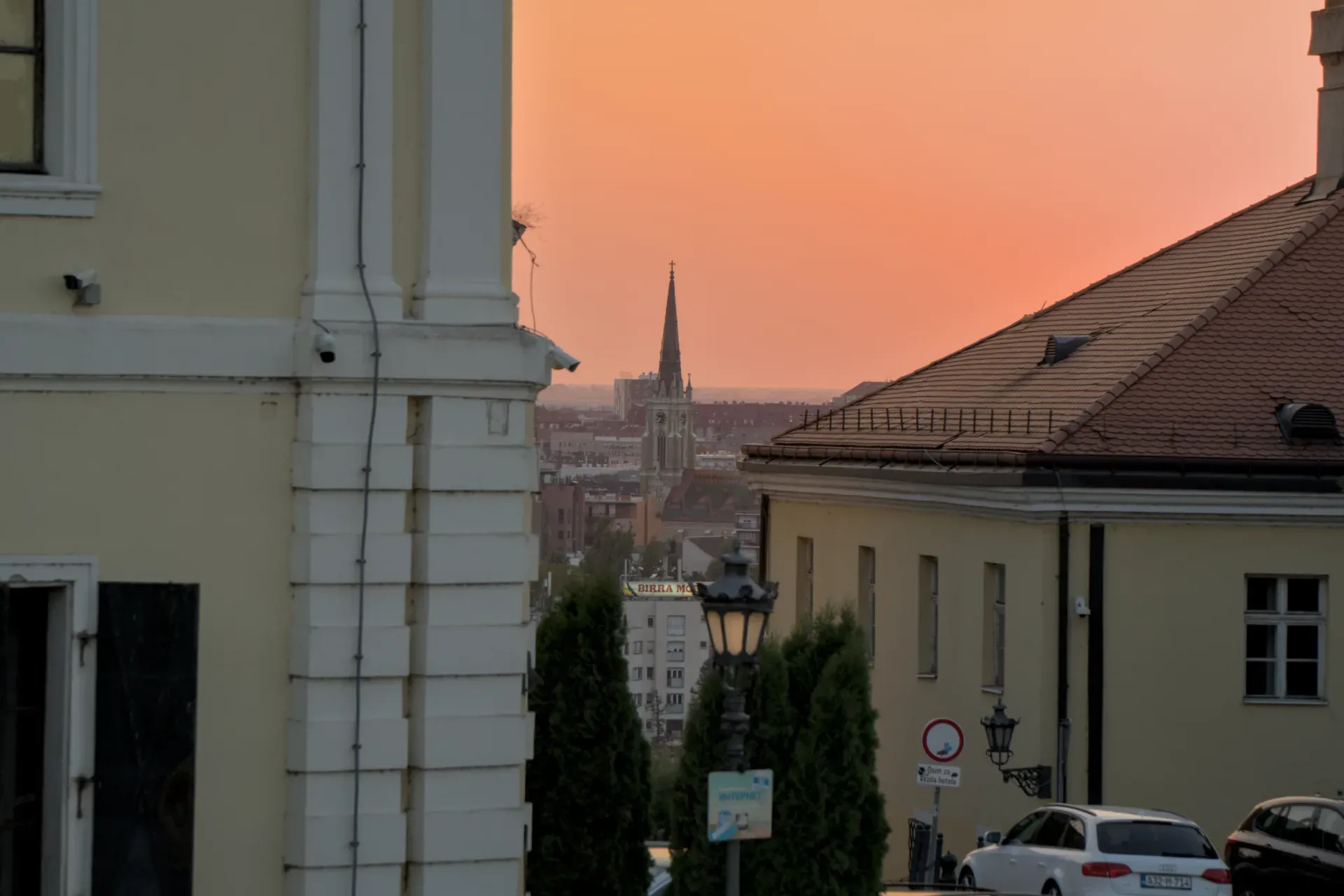 Pogled na Crkvu Srca Isusovog sa prepoznatljivim tornjem, gledano sa Petrovaradinske tvrđave, tokom narandžastog zalaska sunca.