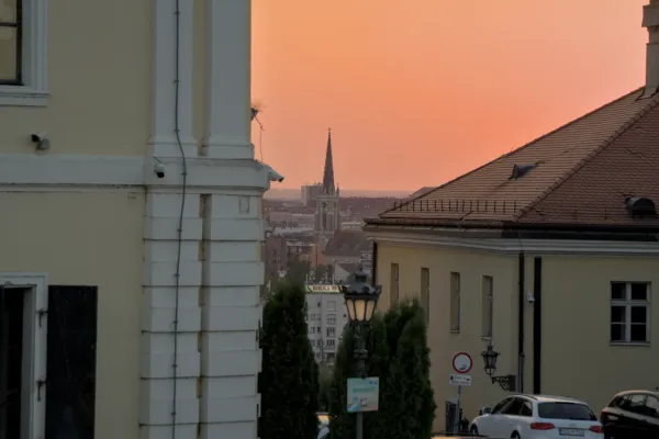 Vista de la Iglesia del Sagrado Corazón con su distintiva aguja, vista desde la Fortaleza de Petrovaradin, durante un atardecer anaranjado.