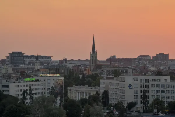 Panorama de Novi Sad al atardecer, visto desde la Fortaleza de Petrovaradin, con torres de iglesias y paisaje urbano.