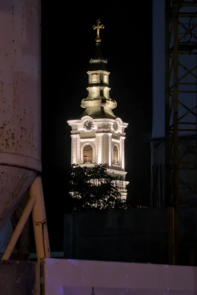 Der beleuchtete Kirchturm der Mariä-Himmelfahrts-Kirche in Novi Sad bei Nacht, umrahmt von dunklem Himmel und moderner Konstruktion.
