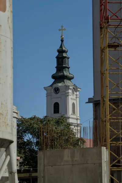 El campanario de la Catedral de la Dormición en Novi Sad se alza contra un cielo azul claro, con su techo verde y cruz dorada.