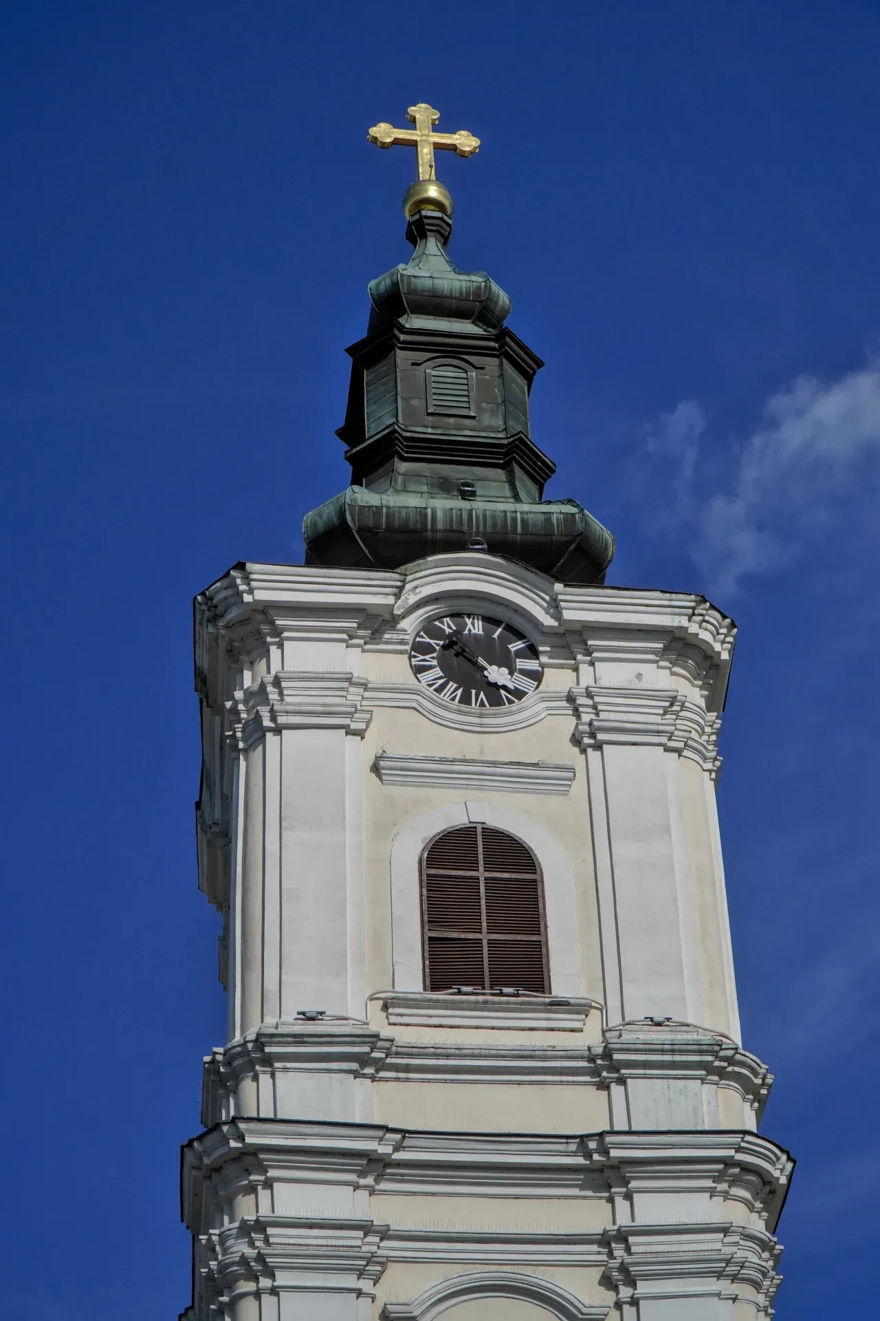Glockenturm der Mariä-Himmelfahrts-Kirche in Novi Sad mit goldenem Turmhelm und Uhr unter blauem Himmel.