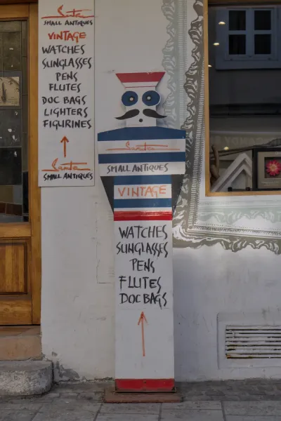 Un letrero pintado a mano para una tienda de antigüedades en Zagreb, que enumera relojes vintage, gafas de sol y otros artículos.
