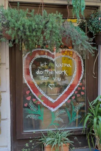Ein handgemaltes Herz mit der Aufschrift 'Let karma do the work for you' auf einem Fenster, umgeben von Pflanzen und herzförmigen Akzenten.