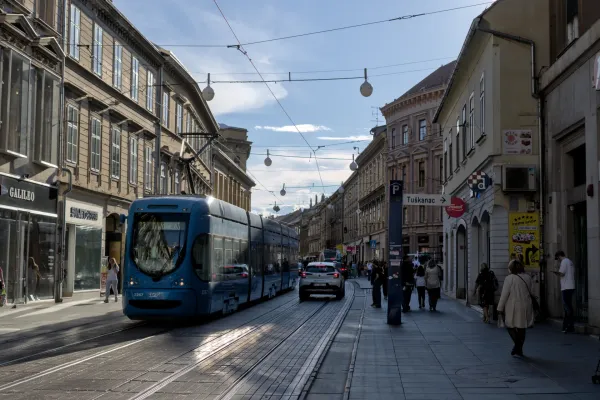 Eine blaue Straßenbahn bewegt sich auf den Gleisen durch eine sonnendurchflutete Straße in Zagreb, Kroatien.