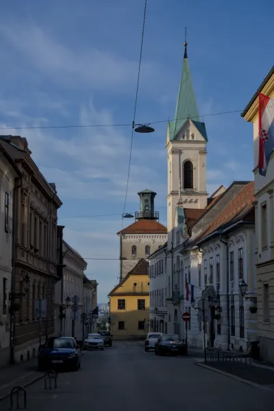 Blick in eine schmale Gasse in Zagreb mit historischen Gebäuden und einem markanten Kirchturm im Hintergrund.