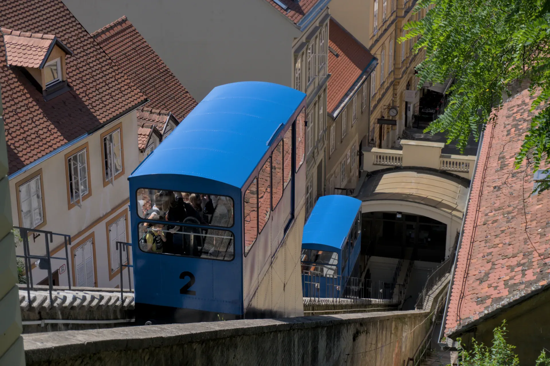 Die blaue Standseilbahn von Zagreb fährt auf einem sonnigen Tag durch die Stadt, mit historischen Gebäuden im Hintergrund.