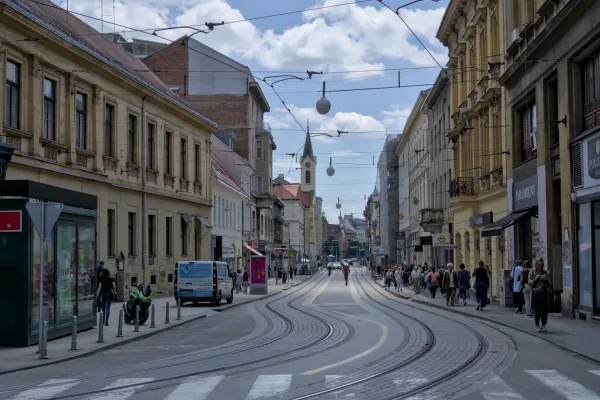 Eine dynamische Aufnahme einer Straße in Zagreb, Kroatien, mit geschwungenen Straßenbahnschienen und historischen Gebäuden, die vom Himmel mit Wolken beleuchtet werden.
