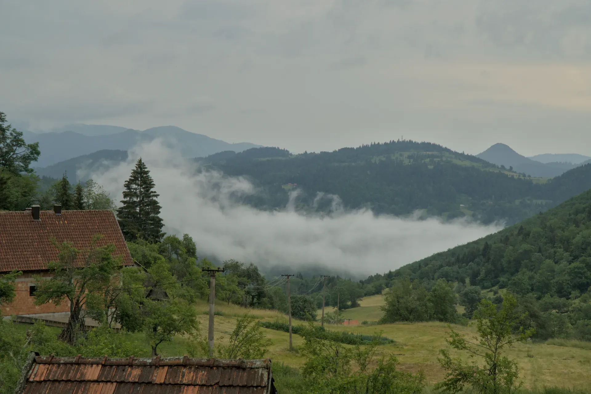 Dichter Nebel steigt in den Bergen des Tara Nationalparks, Serbien, mit einem Ziegelhaus im Vordergrund.