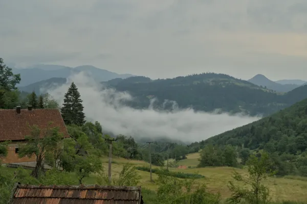 Fitta nebbia che sale sulle montagne del Parco Nazionale di Tara, Serbia, con una casa di mattoni in primo piano.