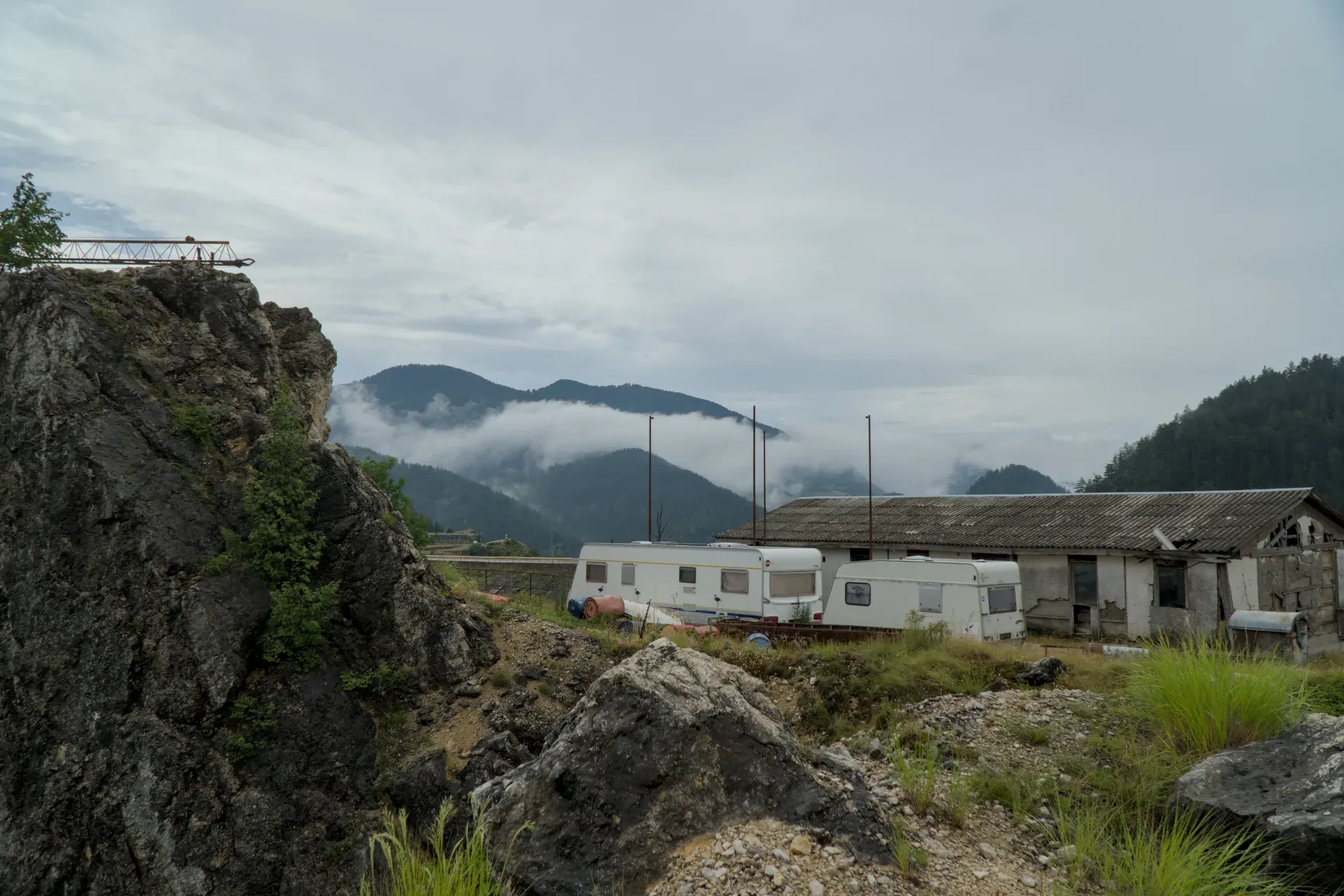 A rough, stormy landscape at Zaovine Lake with caravans and abandoned buildings against misty mountains.