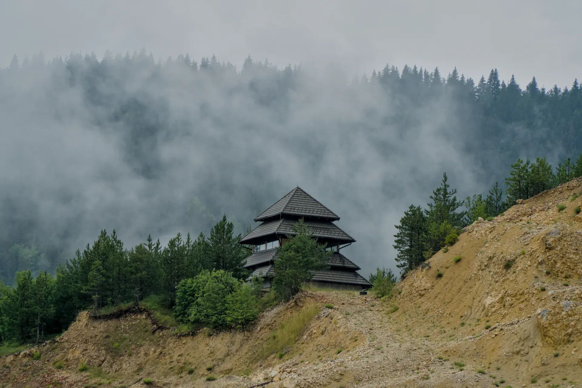 Maison de style pagode sur une colline au-dessus du lac Zaovine dans le parc national de Tara, entourée de pins et de brume.