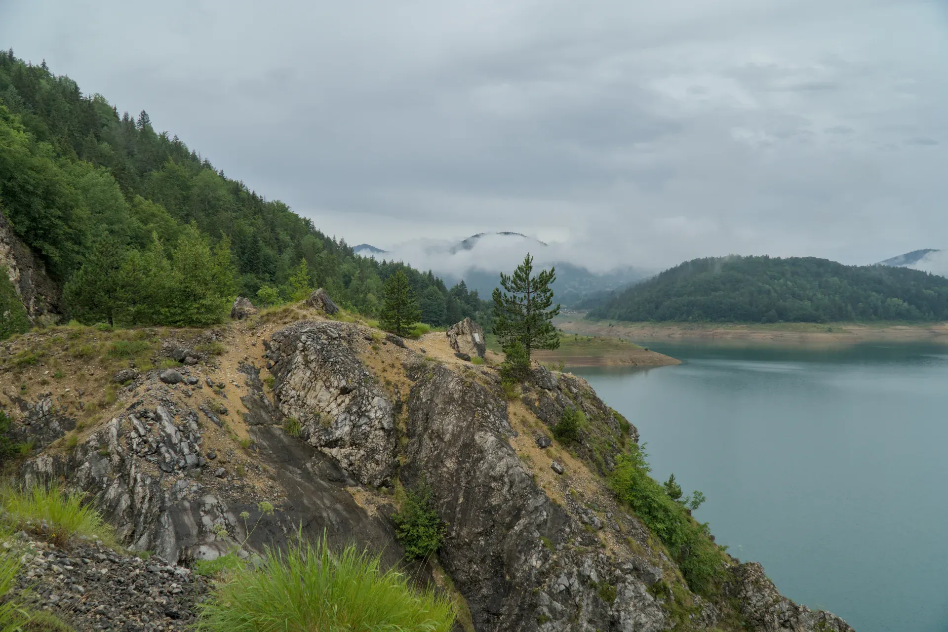 Le lac Zaovine, entouré de falaises abruptes et traversé par des volutes de brouillard, offre un spectacle naturel majestueux.