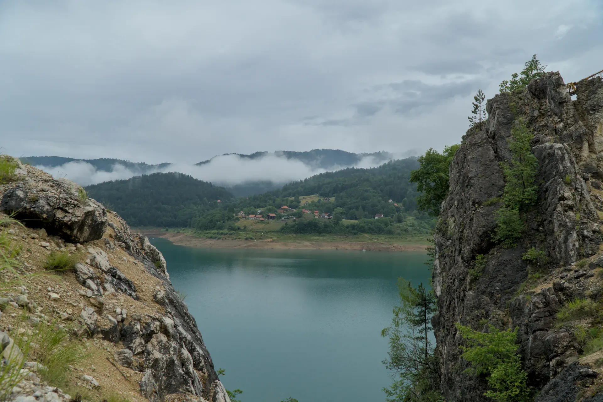 Panorama del lago Zaovine tra rocce scoscese, con colline boscose e nebbia sullo sfondo.