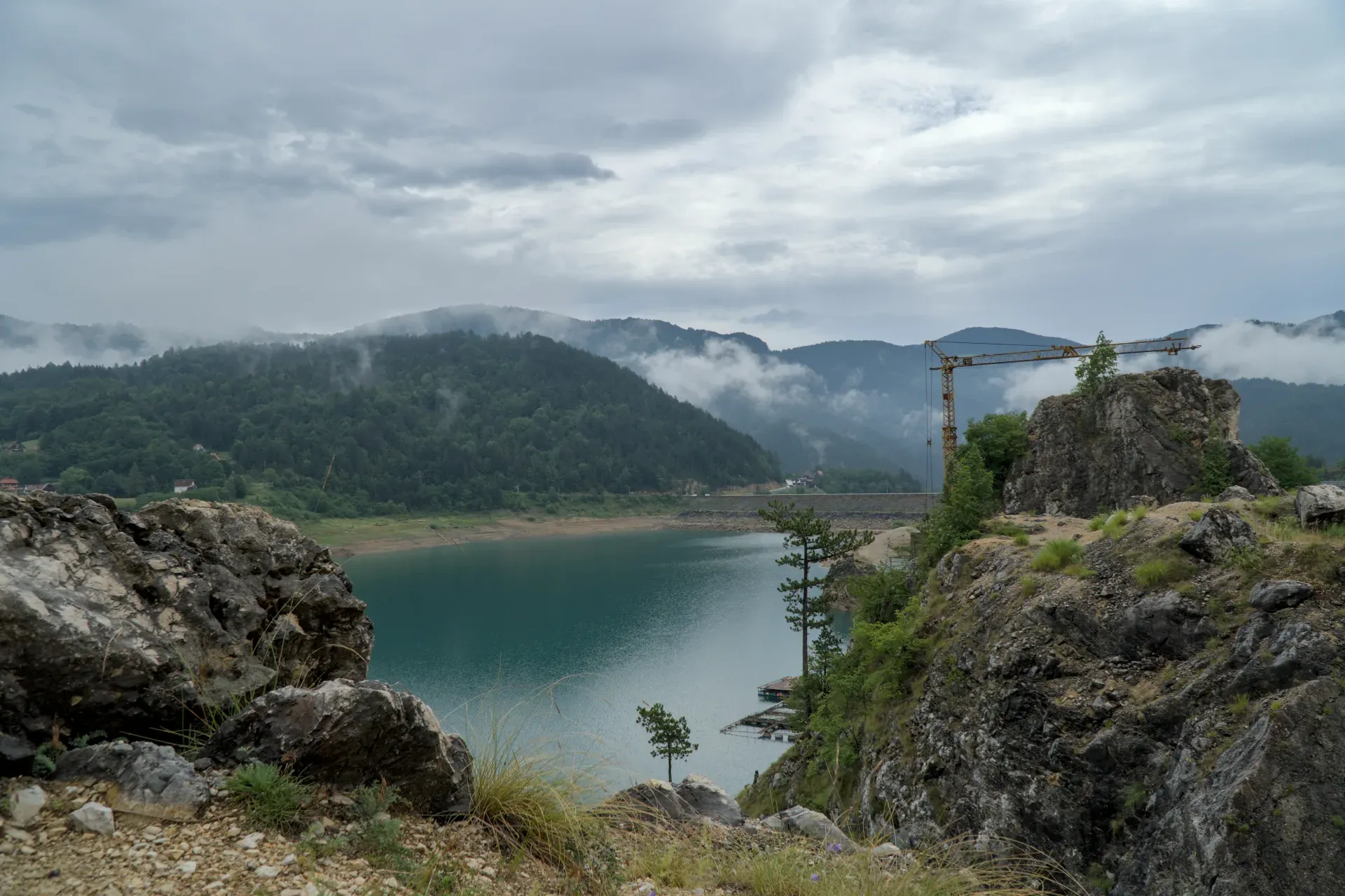Paysage brut au lac Zaovine avec brouillard et nuages, encadré par des rochers, des arbres et des montagnes.