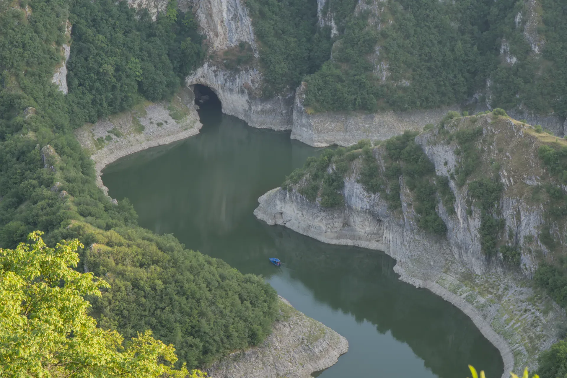Le canyon d'Uvac en Serbie présente des méandres sinueux de rivière et la grotte d'Ušačka, avec un petit bateau bleu dans l'eau.