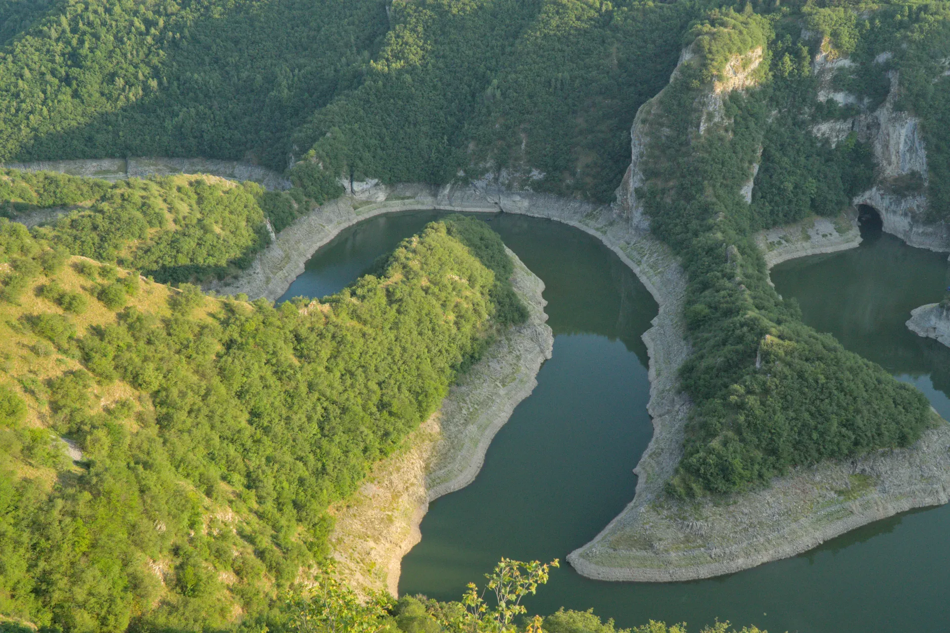 A winding riverbed under the setting sun, surrounded by green hills in Serbia.