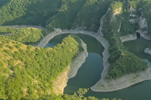 Ein auswindendes Flussbett unter der untergehenden Sonne, umgeben von grünen Hügeln in Serbien.